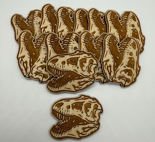 Set of 12 laser engraved dinosaur skull wooden bobbins on white background, detailed T-rex skull design on birch plywood