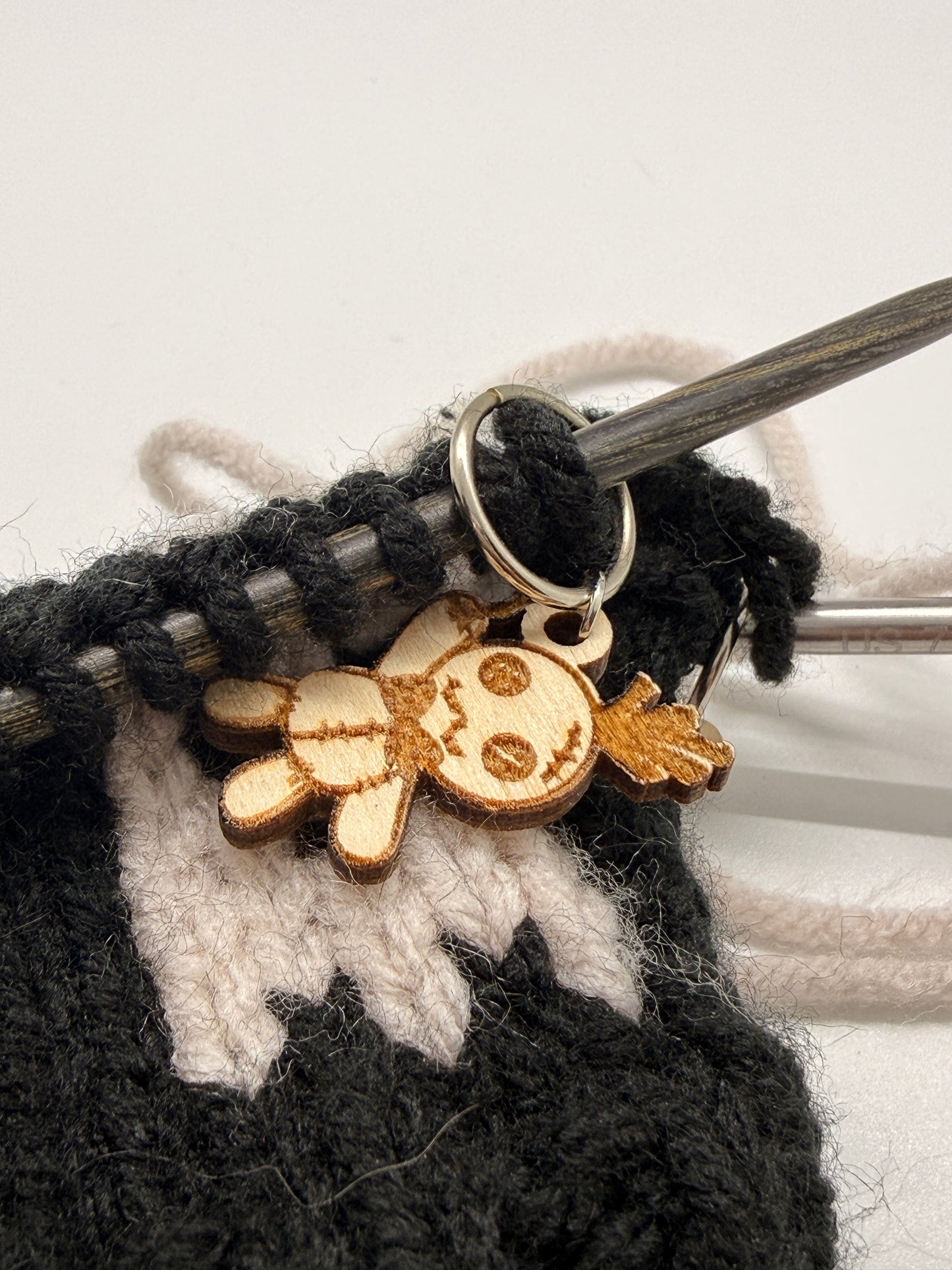 Wooden charm attached to a knitting needle with yarn.