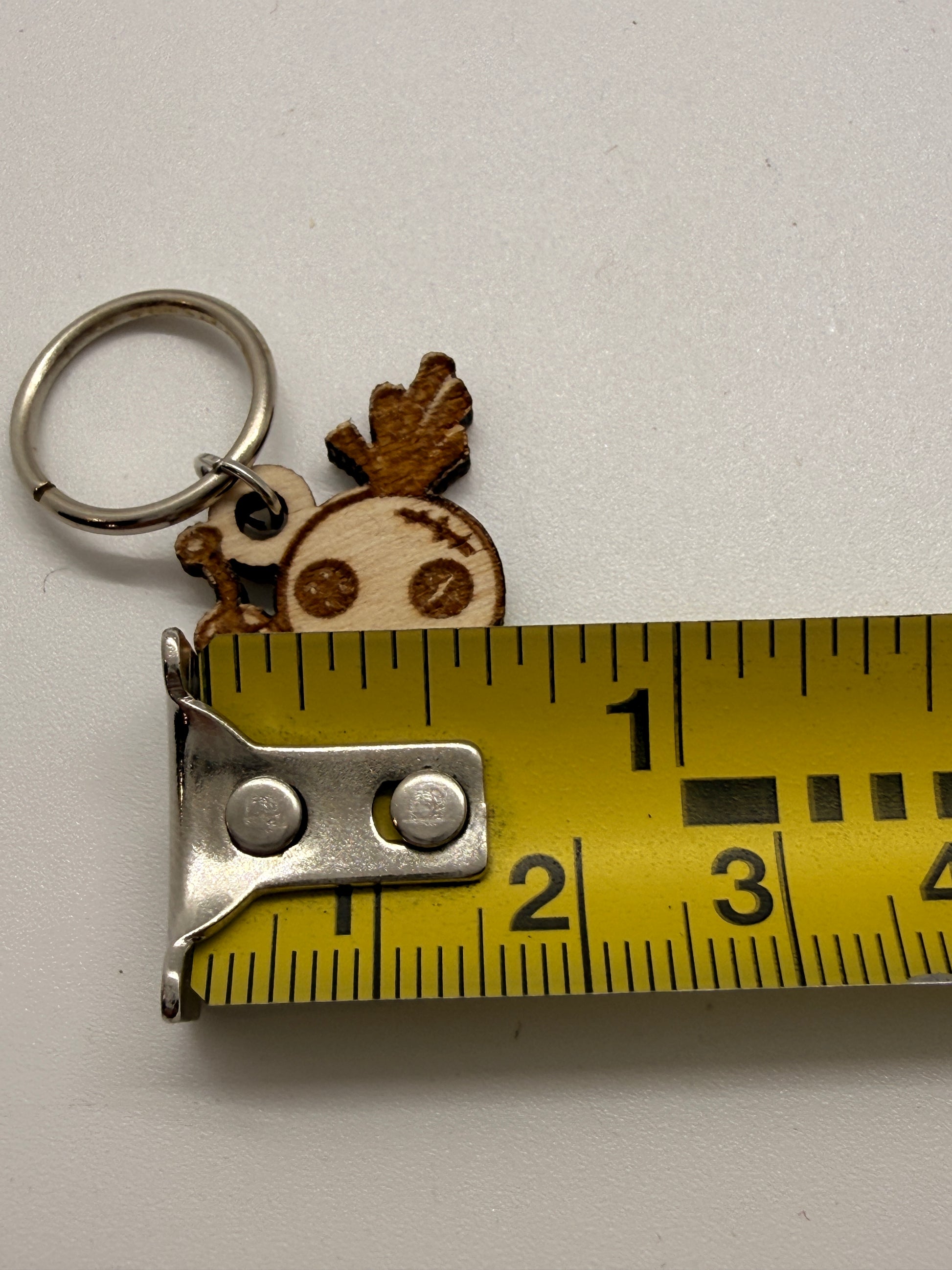 Keychain with a small  design next to a measuring tape on a white background