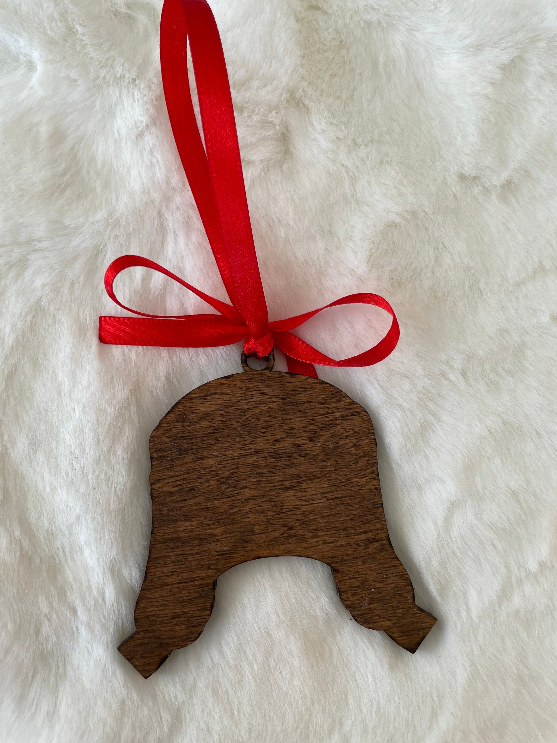 Wooden bell ornament with a red ribbon on a white fur background