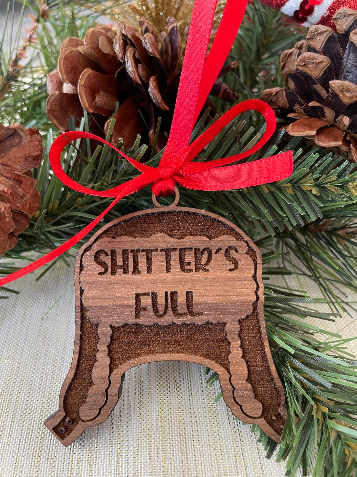 Wooden ornament with 'SHITTER'S FULL' text on a Christmas tree background