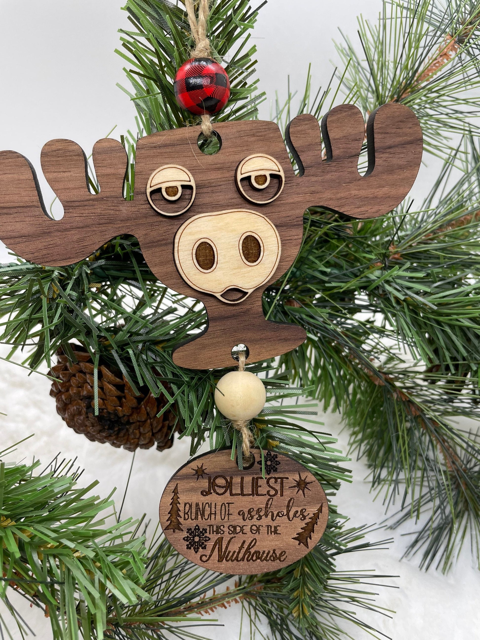 Wooden moose ornament with a humorous tag on a Christmas tree.