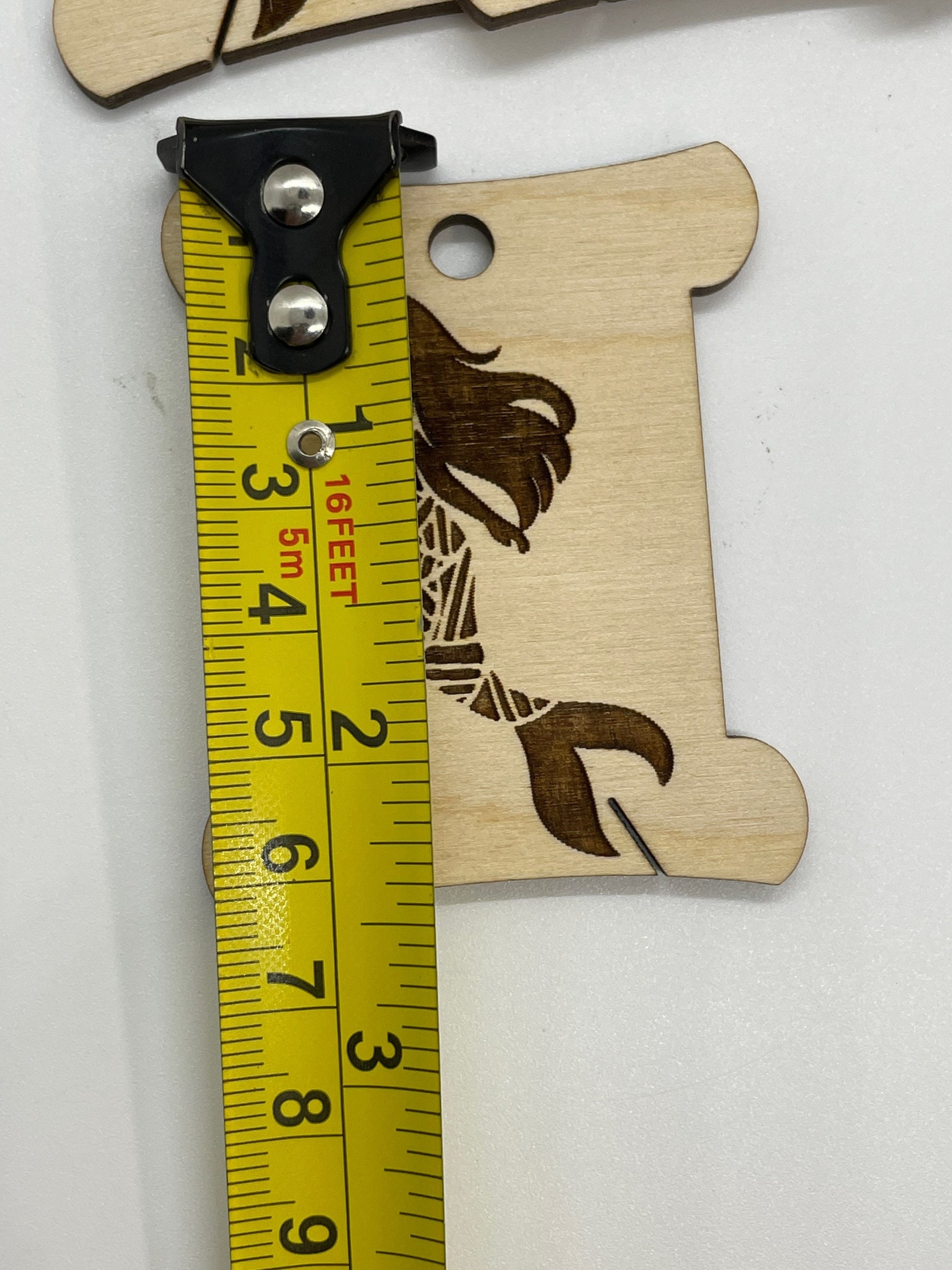 Wooden bobbin with mermaid design and measuring tape for scale on a white background