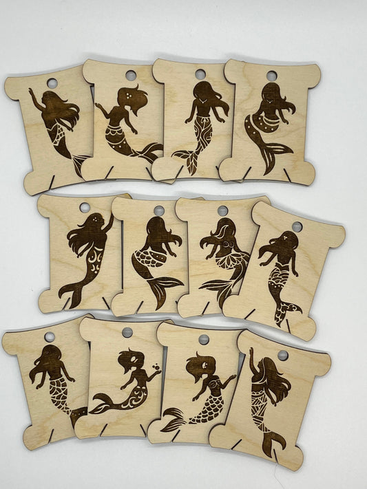 Set of wooden bobbins with mermaid designs on a white background