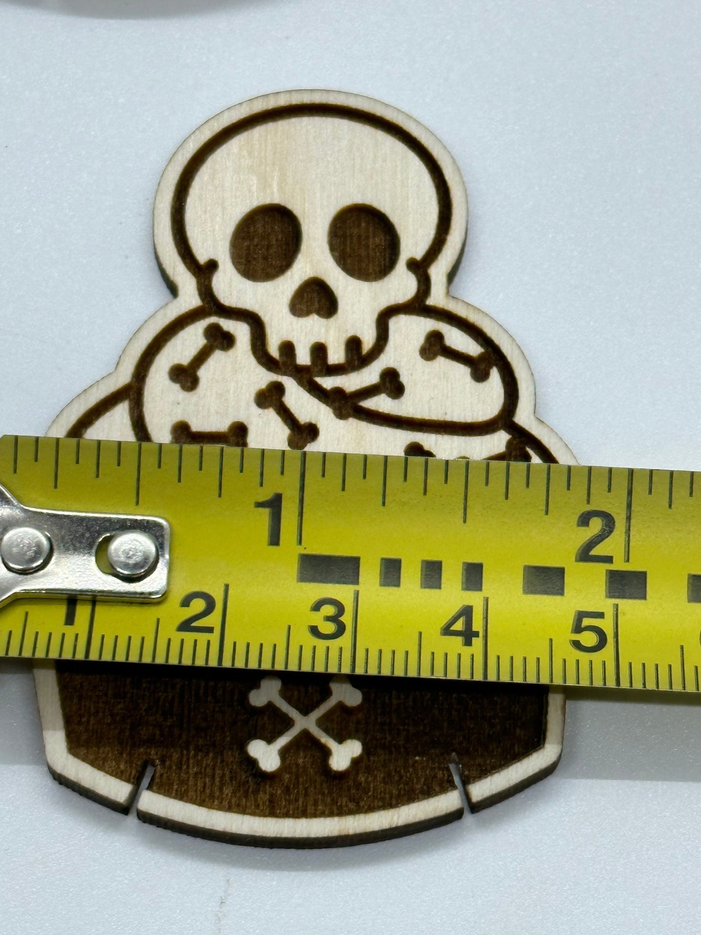 Wooden skull and crossbones patch with a measuring tape for scale on a white background