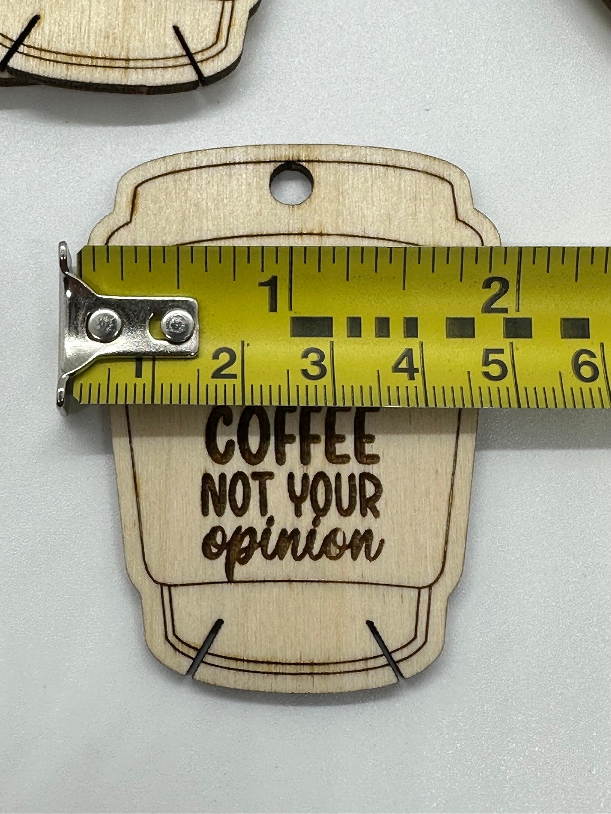 Wooden keychain with 'Coffee Not Your Opinion' text and measuring tape for scale on a white background