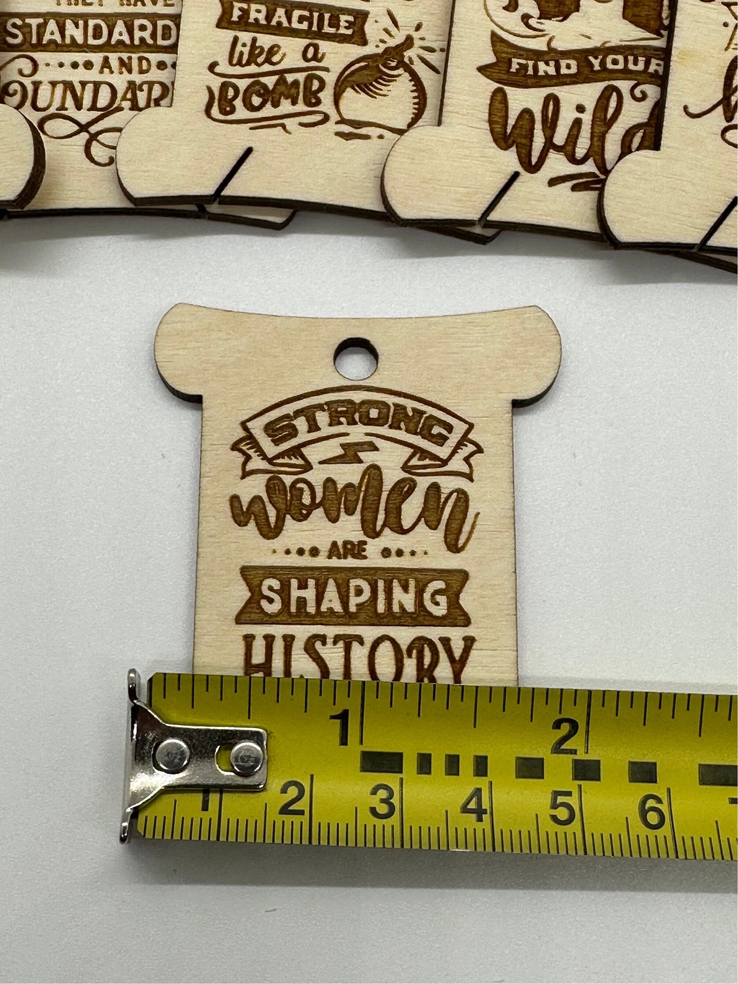 Wooden tag with 'Strong women are shaping history' text, measured against a ruler.