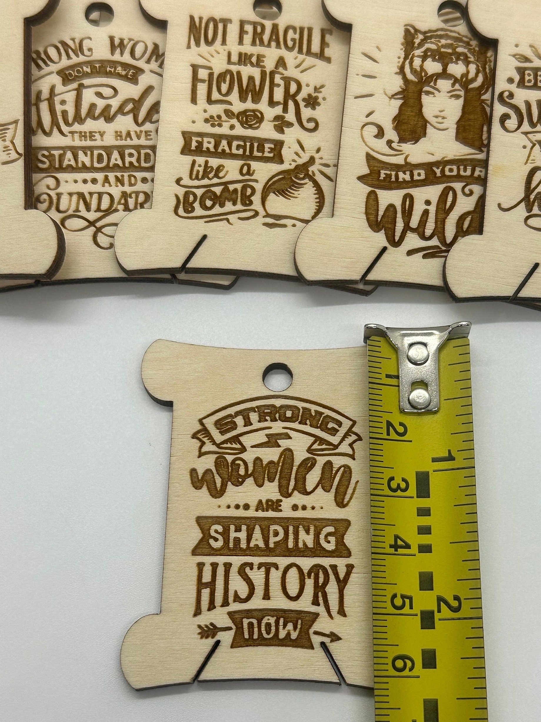 Wooden tags with motivational phrases and a measuring tape for scale on a white background