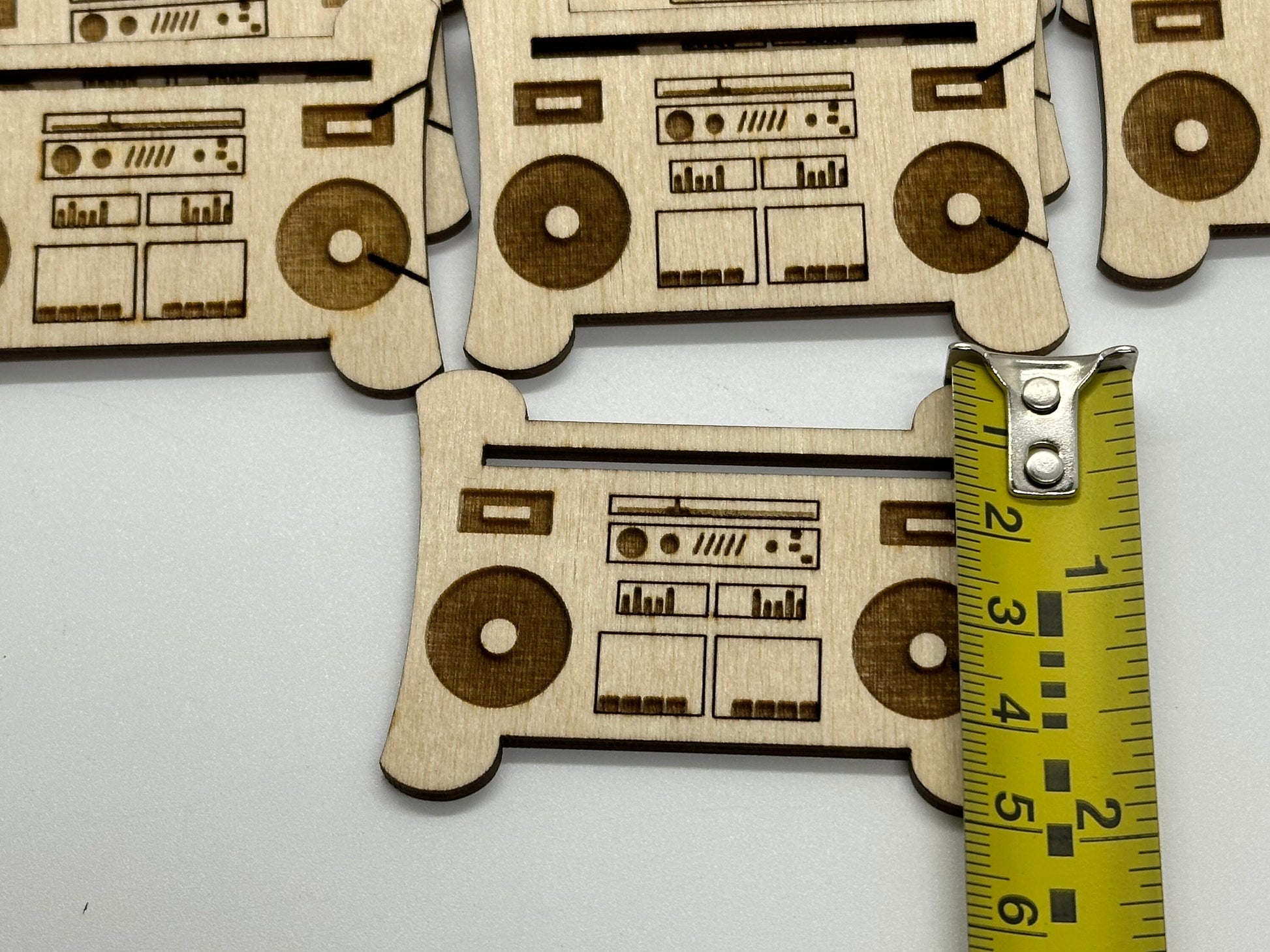 Wooden boombox-shaped cutouts with laser engraving next to a measuring tape on a white background