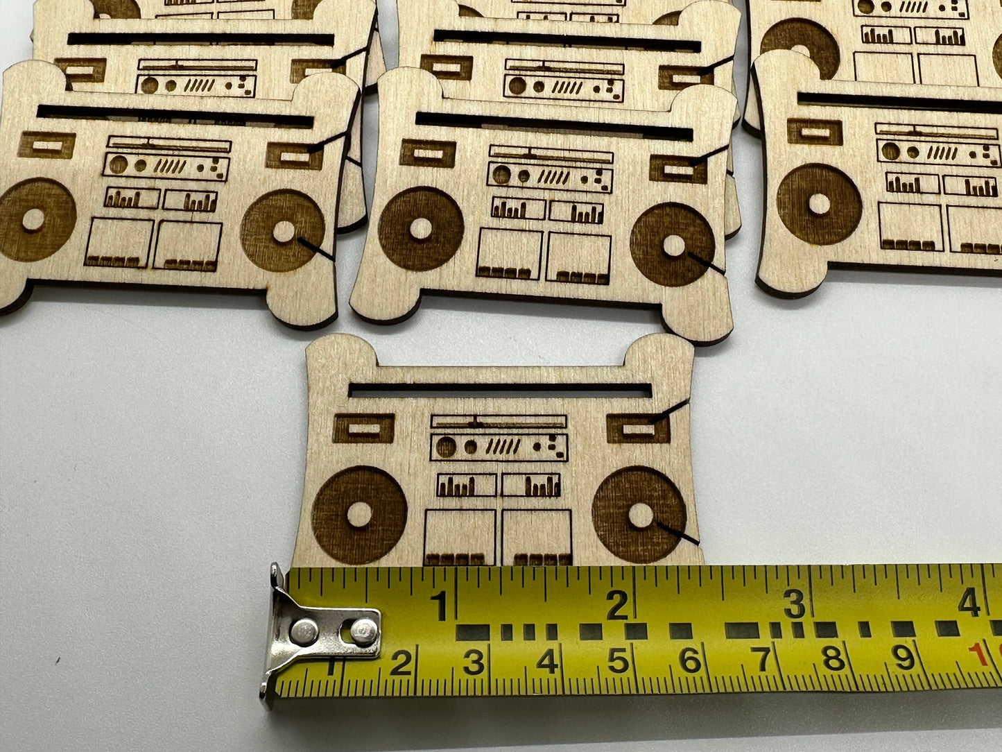 Wooden cutouts of boomboxes with a tape measure for scale on a white background