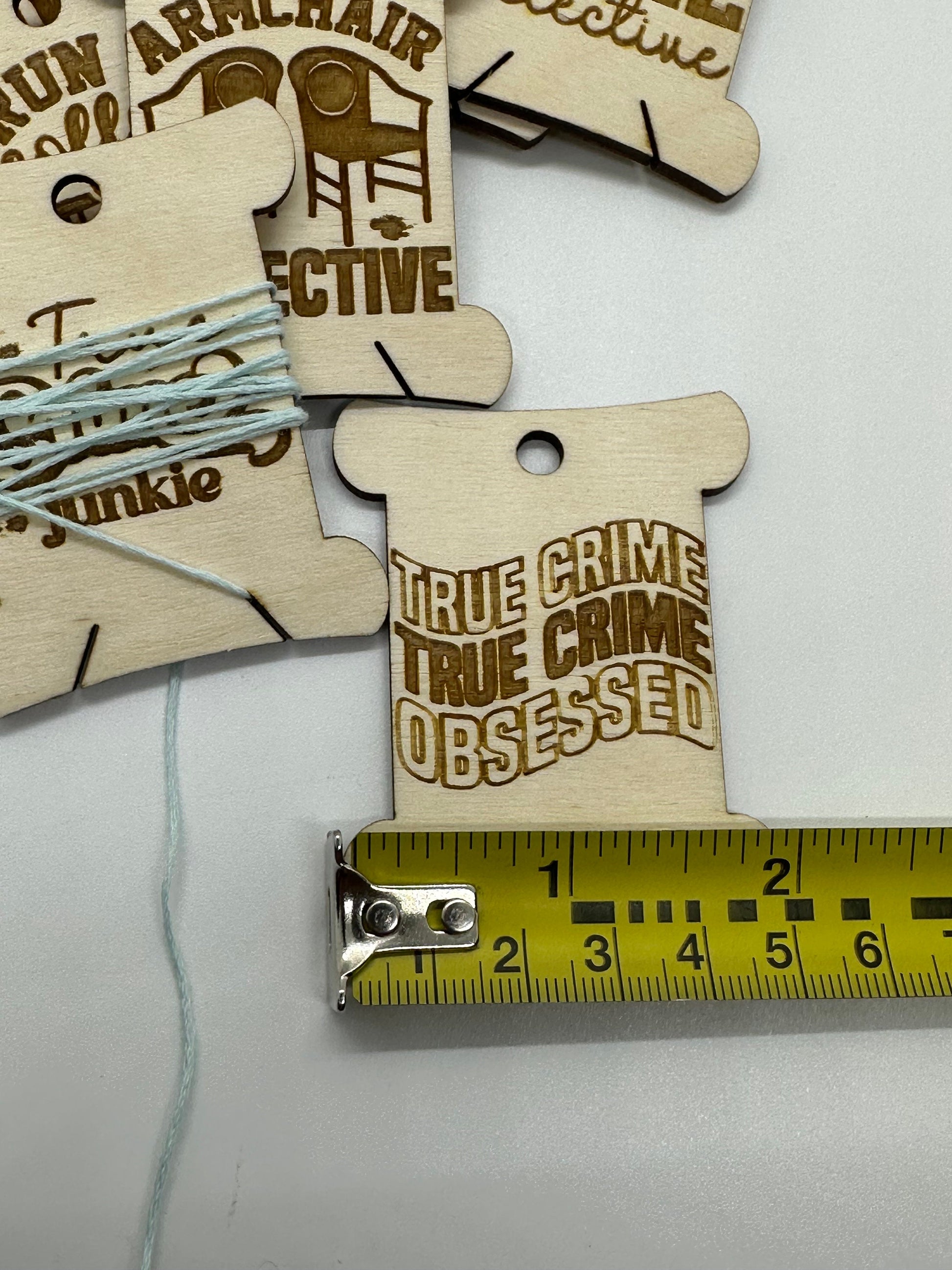 Wooden tags with 'True Crime True Crime Obsessed' text and a measuring tape for scale.