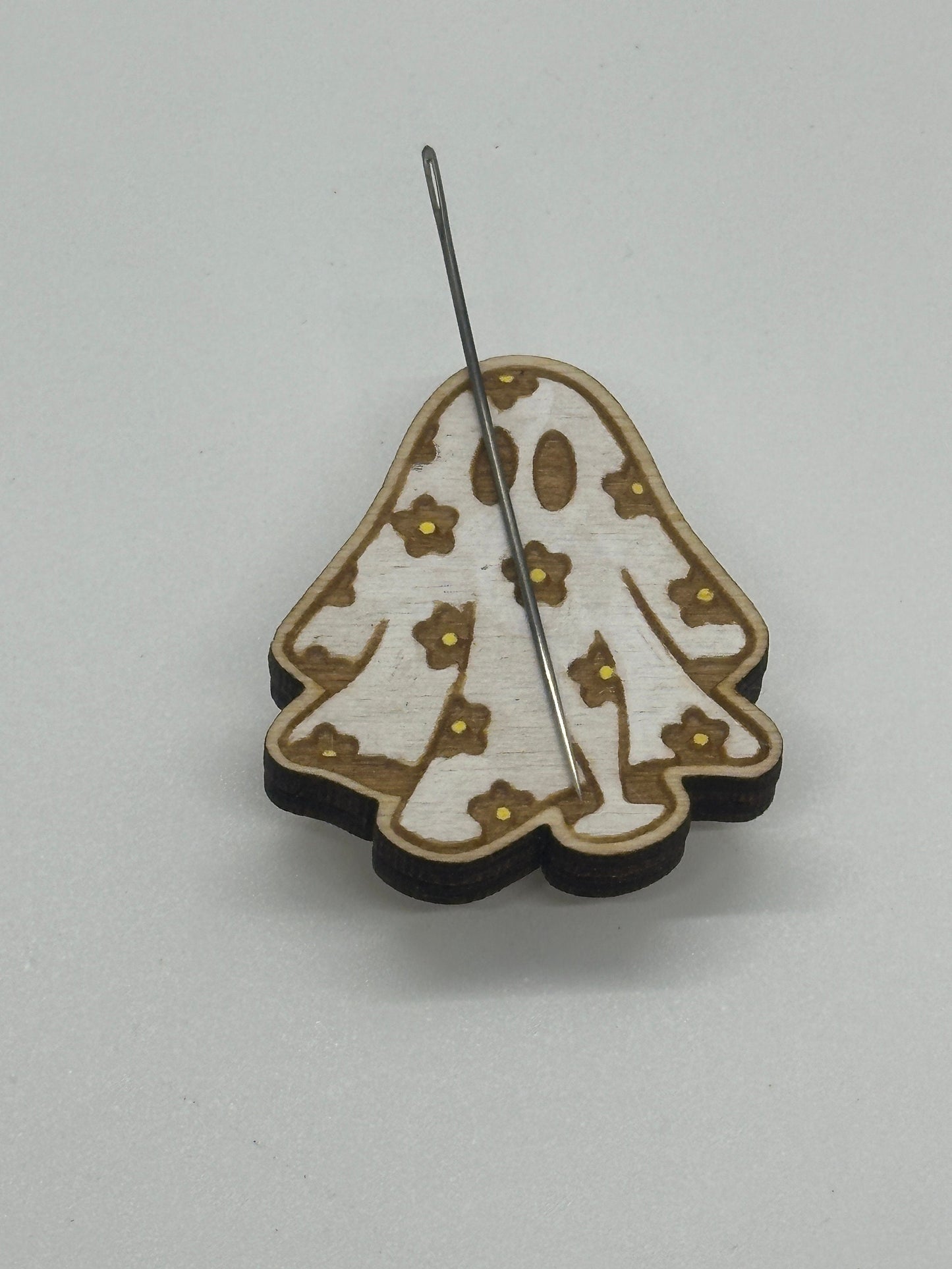 Wooden ghost-shaped minder with needle and  flower patterns on a light gray background