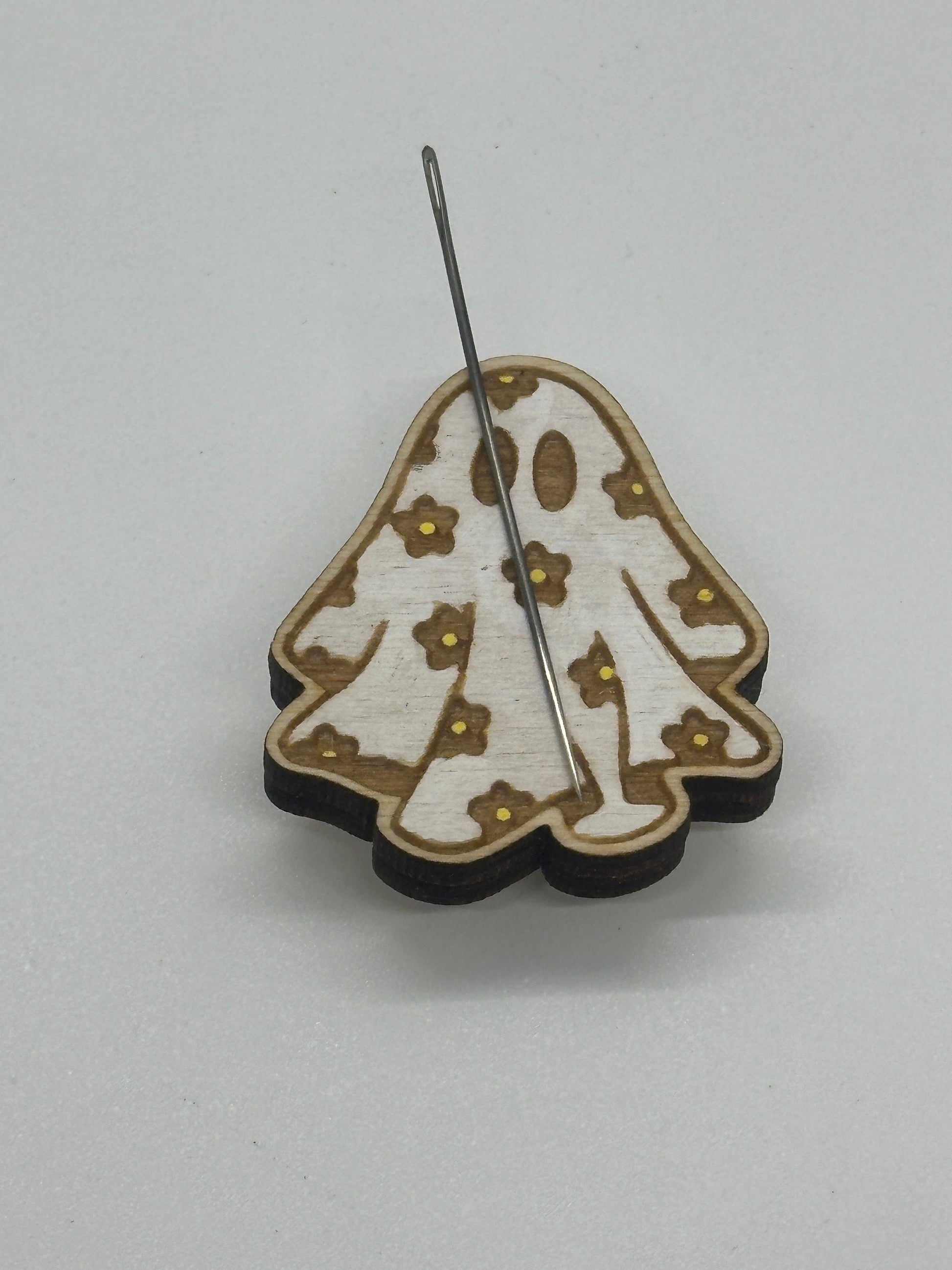 Wooden ghost-shaped minder with needle and  flower patterns on a light gray background