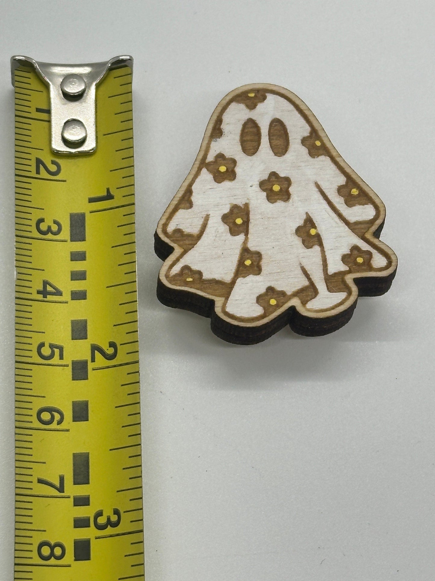 Decorative wooden piece with floral patterns on a white background, measured against a tape measure.