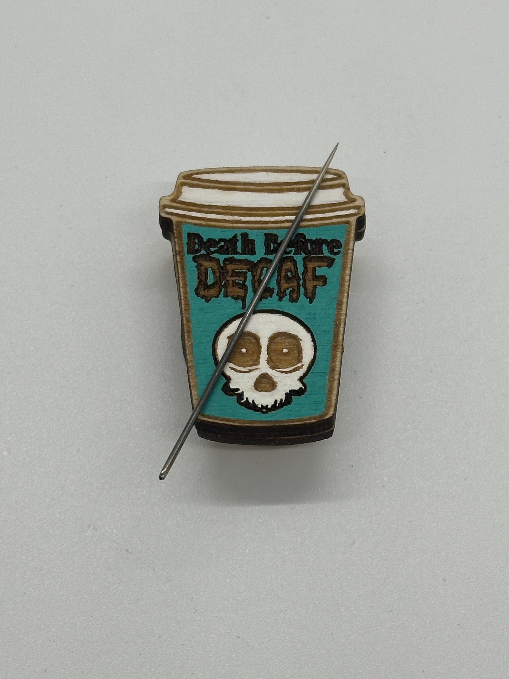 Pin with coffee cup design and skull illustration on a gray background