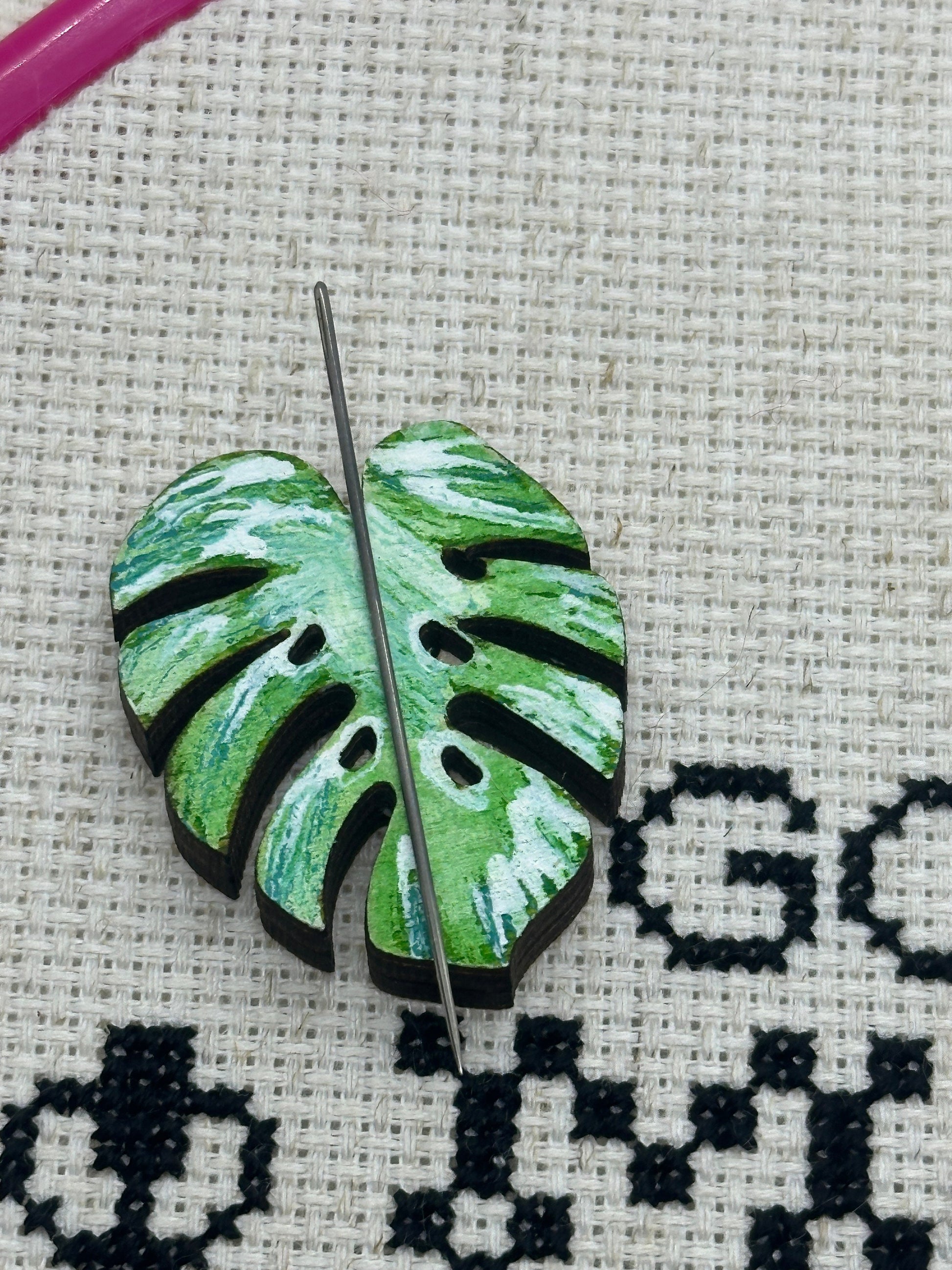 Embroidery hoop with a green leaf-shaped embroidery design on a cross-stitched background.