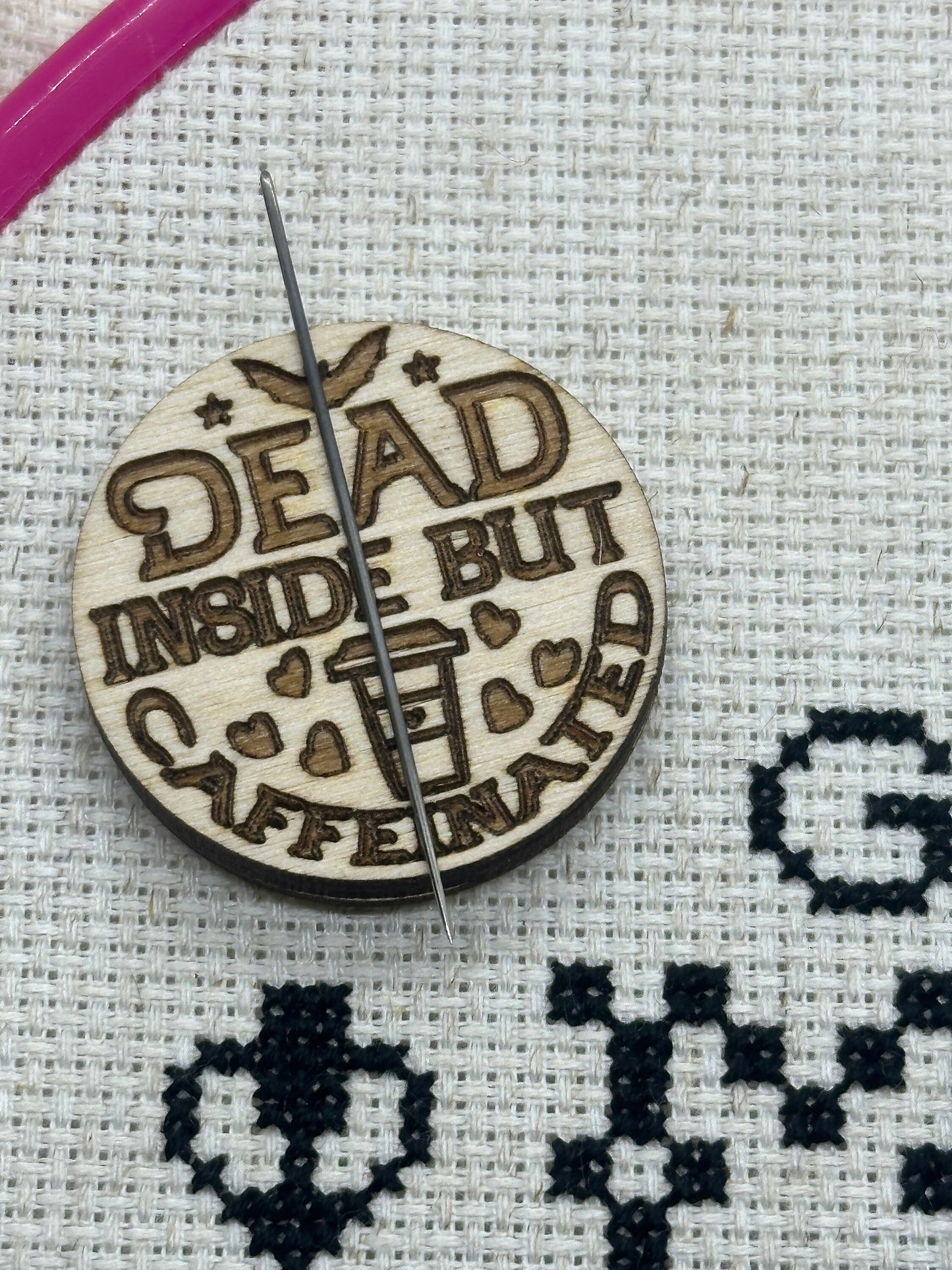 Wooden round badge with 'Dead Inside But Caffeinated' text on a cross-stitched background