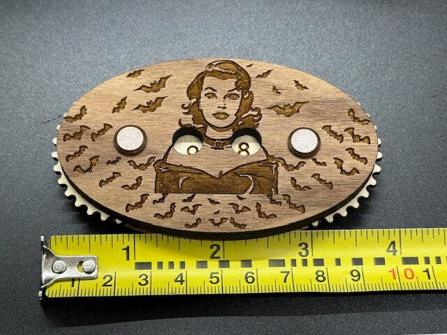 Wooden counter with engraved design of a woman and bats, next to a measuring tape for scale.