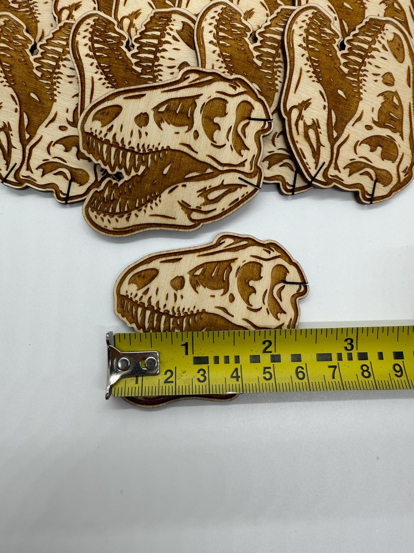 Dinosaur skull-shaped wooden cutouts with a measuring tape for scale on a white background