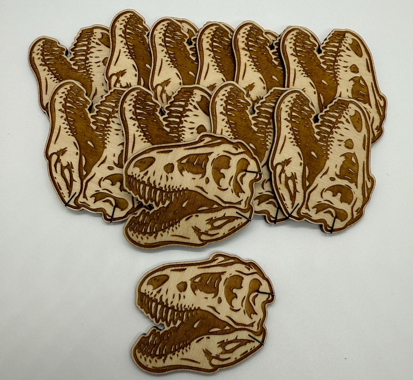 Set of 12 laser engraved dinosaur skull wooden bobbins on white background, detailed T-rex skull design on birch plywood